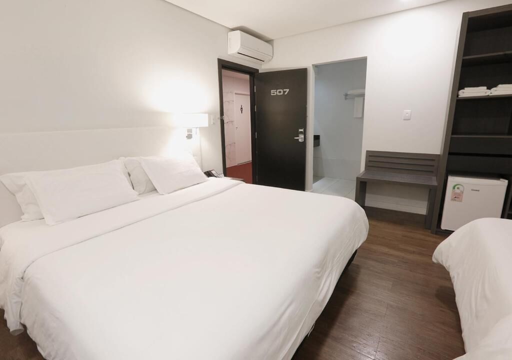 A hotel room with a bed, a desk, a wardrobe, and an air conditioning unit.