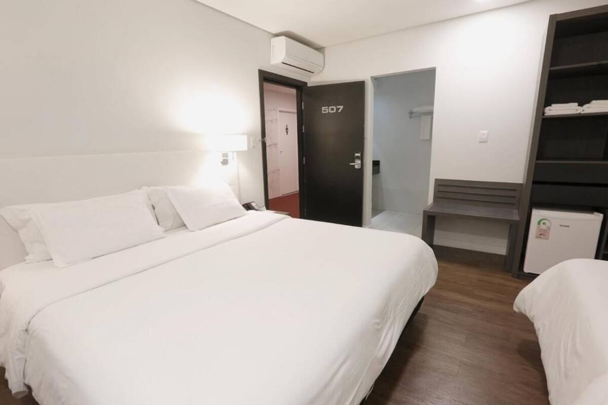 A hotel room with a bed, a desk, a wardrobe, and an air conditioning unit.