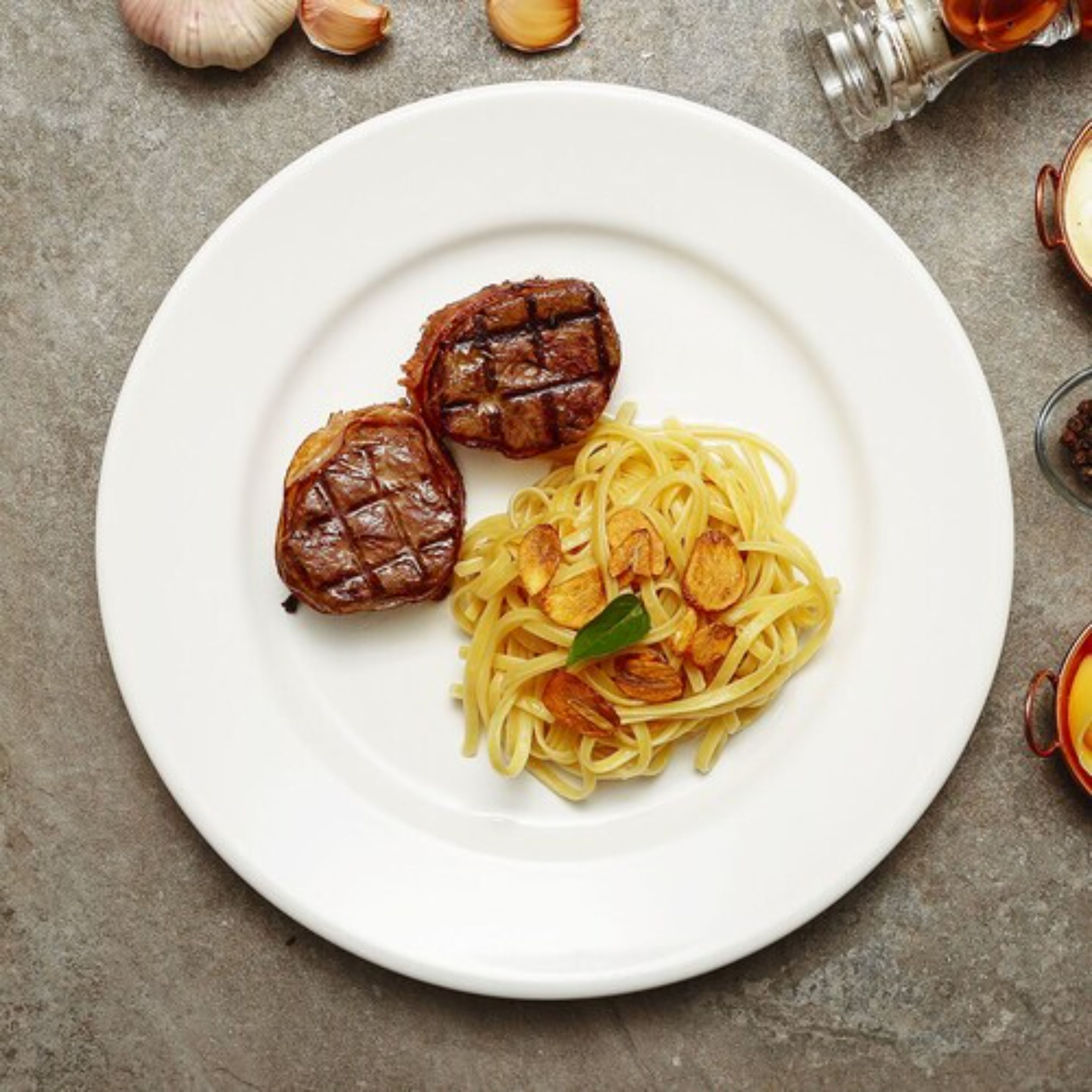 Lautasella on spagettia ja kaksi grillattua lihapullaa, ja lautanen on valkoinen.