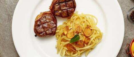Lautasella on spagettia ja kaksi grillattua lihapullaa, ja lautanen on valkoinen.