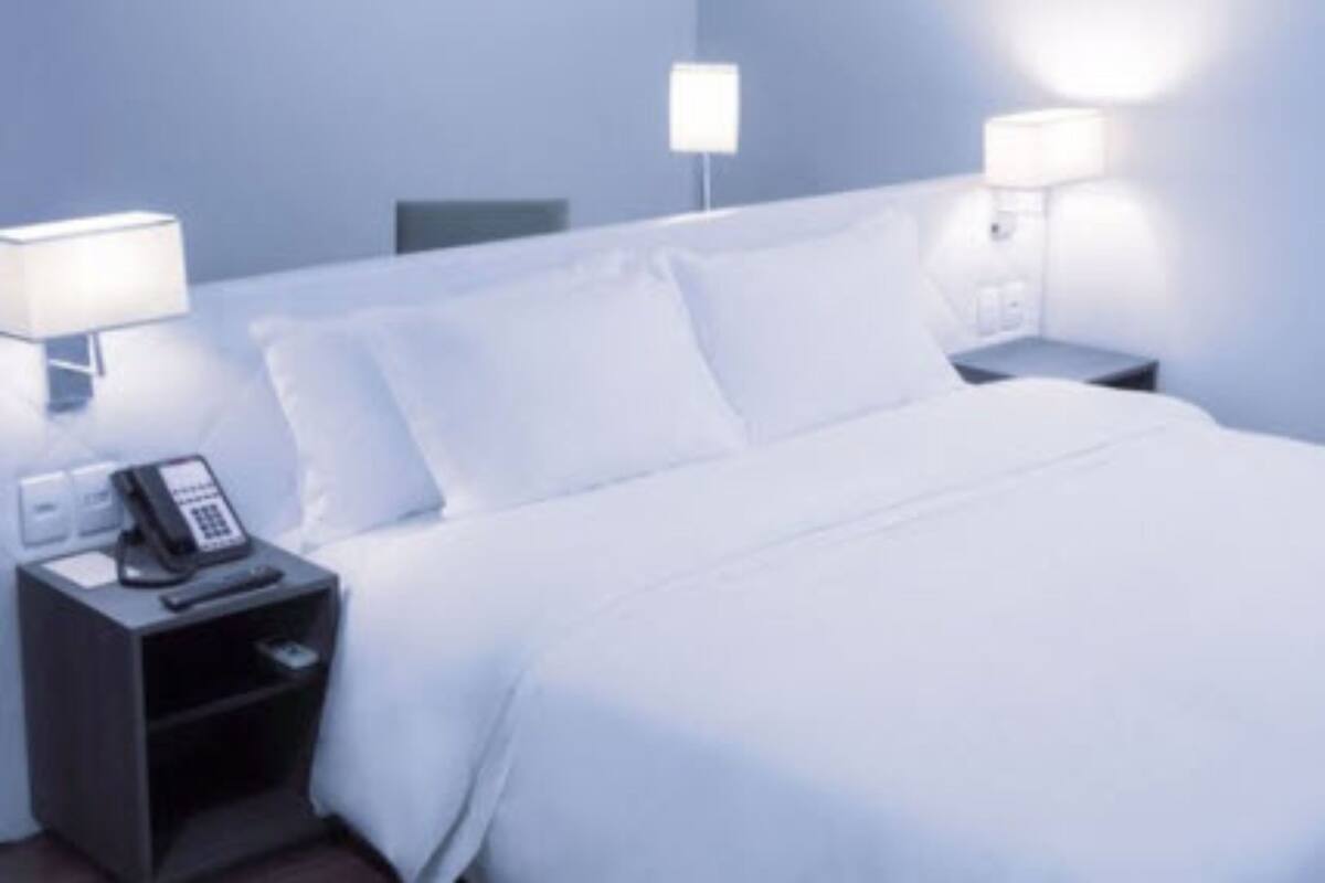 A hotel room with a neatly made bed, a bedside telephone, and two wall-mounted lamps.