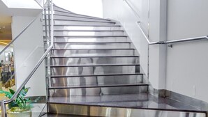 A modern staircase with metallic steps and glass railings, leading to an upper floor. - Fratele Business (Patos de Minas)