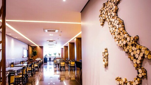 A modern hotel corridor with a long dining area, wooden wall art, and a polished floor. - Fratele Business (Patos de Minas)