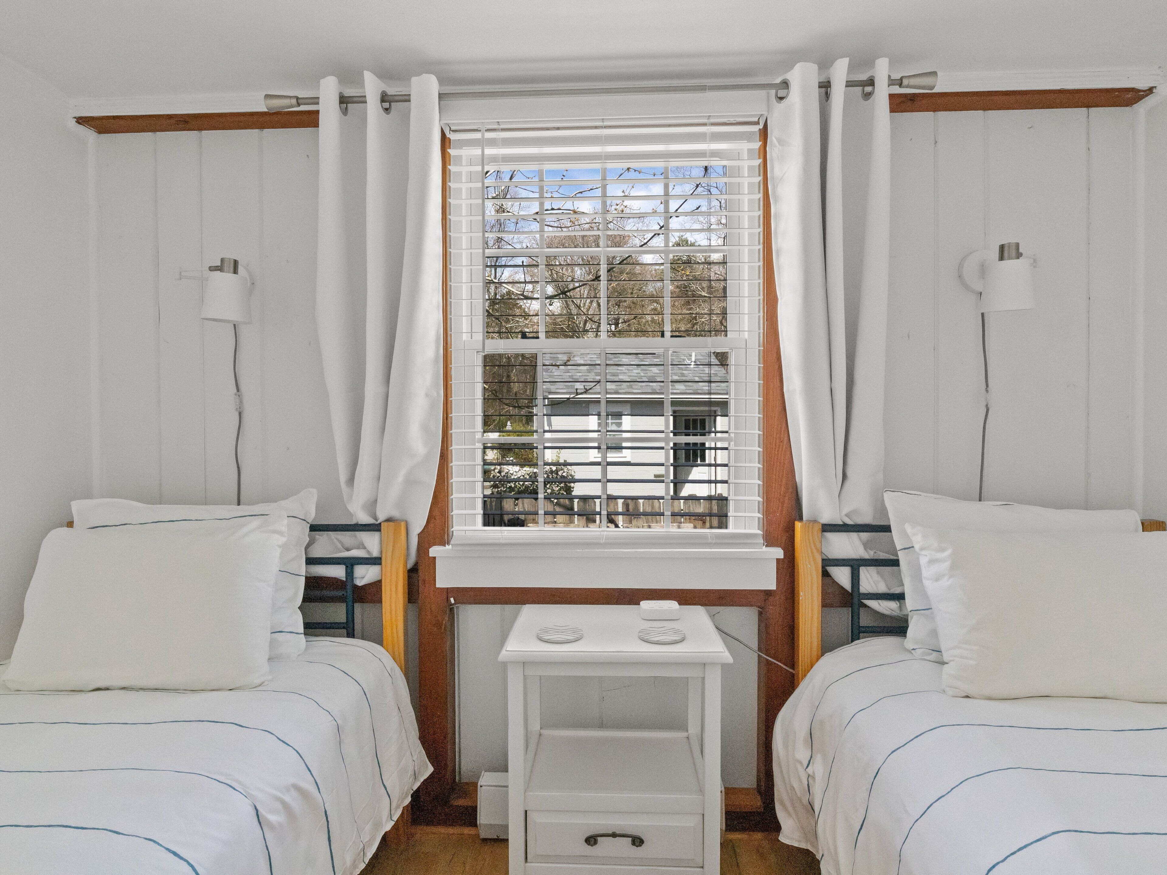 Une chambre avec deux lits, une petite table avec une lampe et une fenêtre avec des stores.