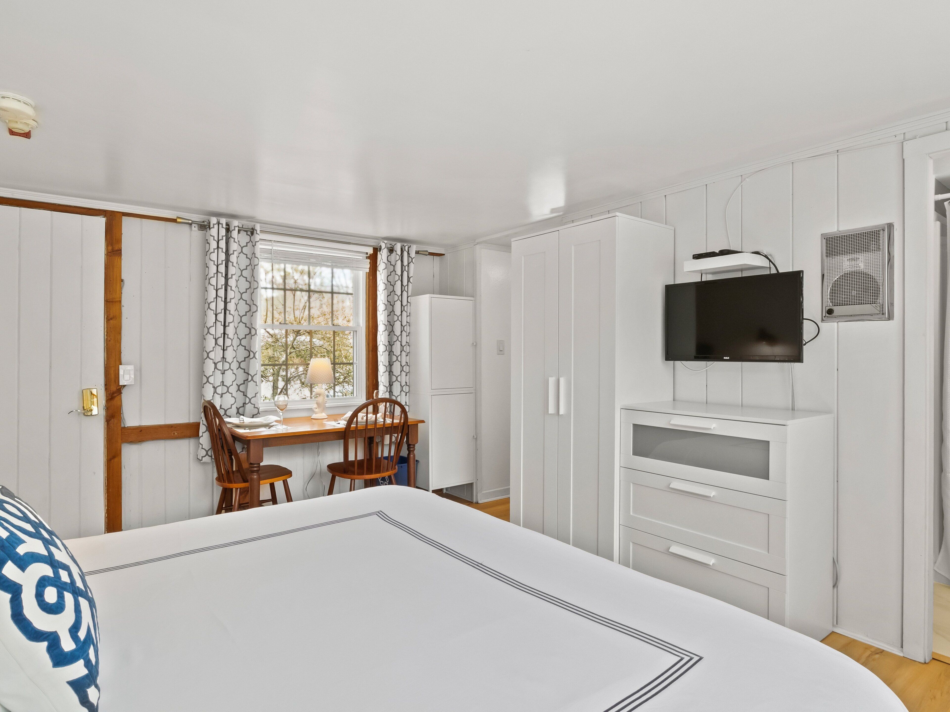 Een slaapkamer met een bed, een bureau met stoelen, een televisie en een kledingkast.