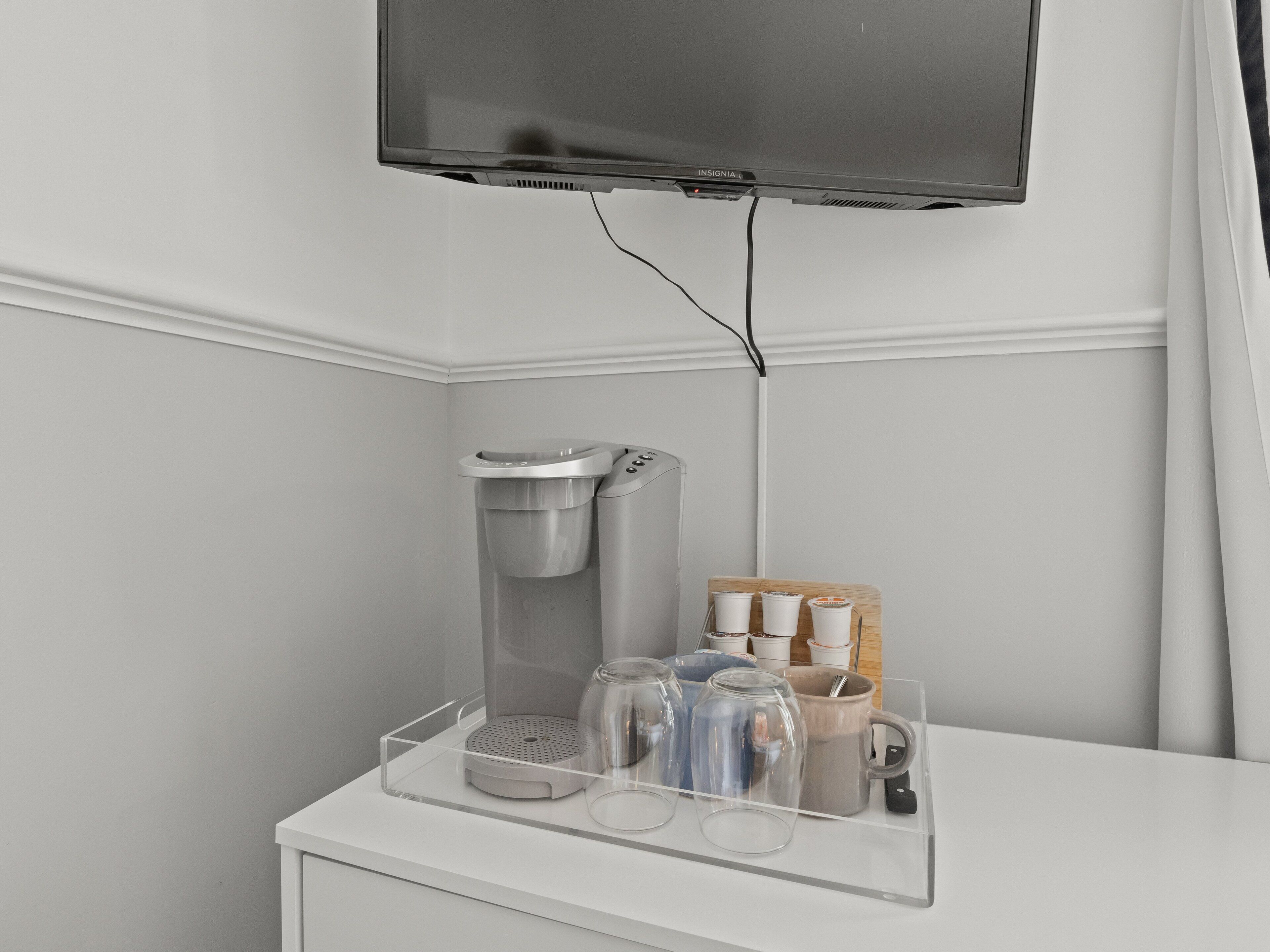 Een moderne badkamer met een koffieapparaat, een glazen koffiehoek en een bevestigde televisie.