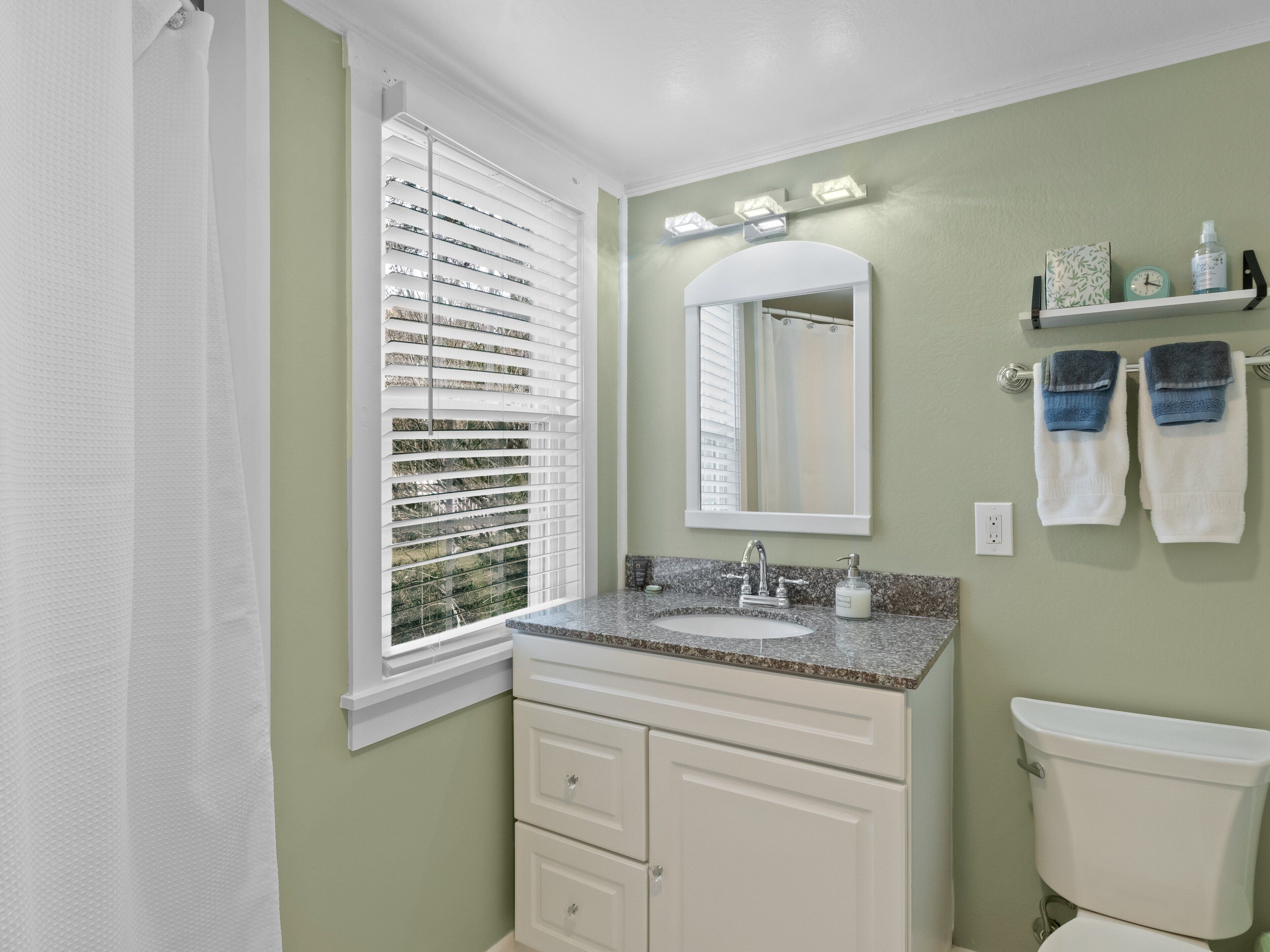 A bathroom with a window, a sink, a mirror, a toilet, and a shelf with towels.