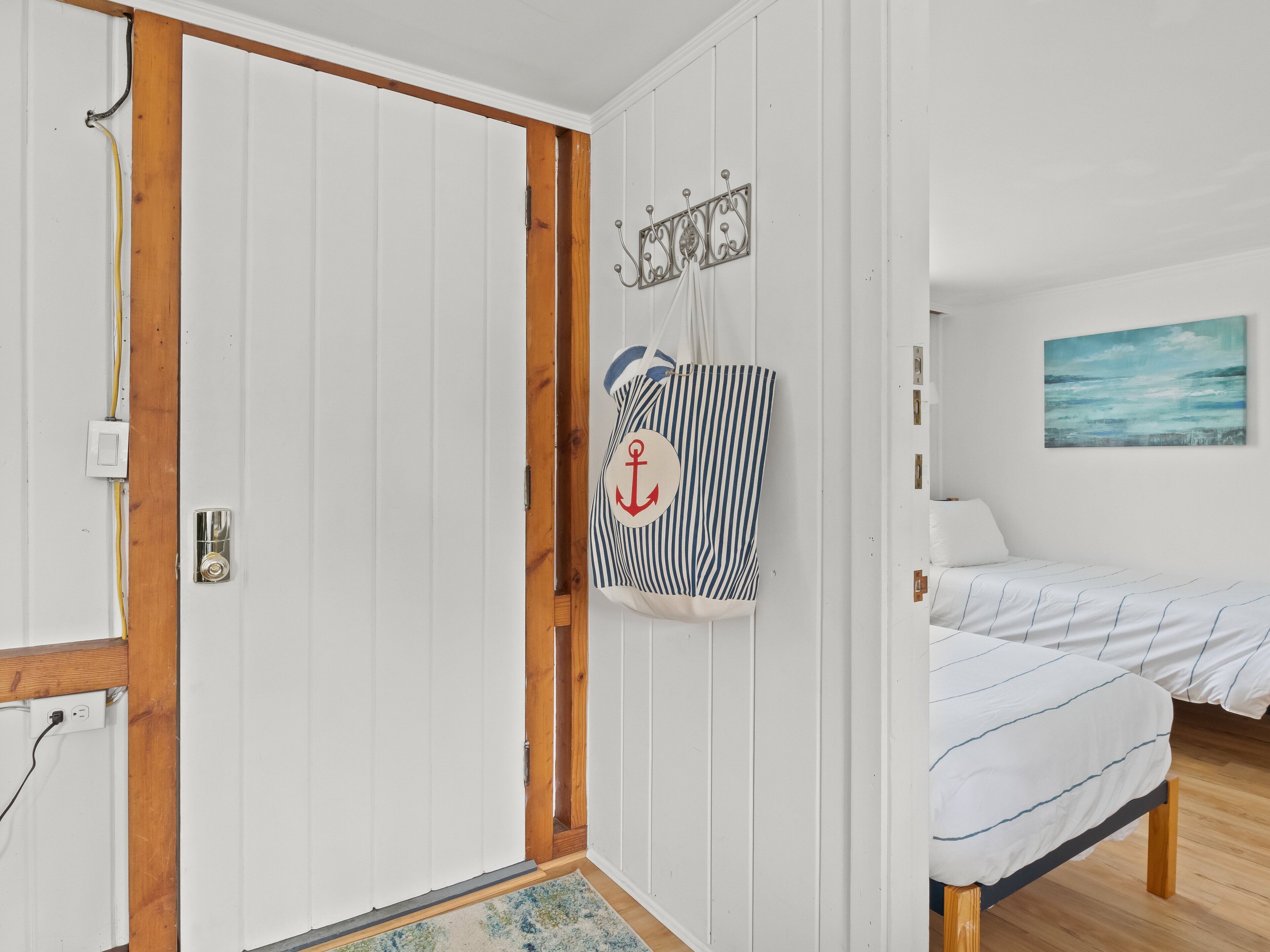 A bedroom with a bed, a wooden floor, a white door, and a wall-mounted coat rack with a striped bag.