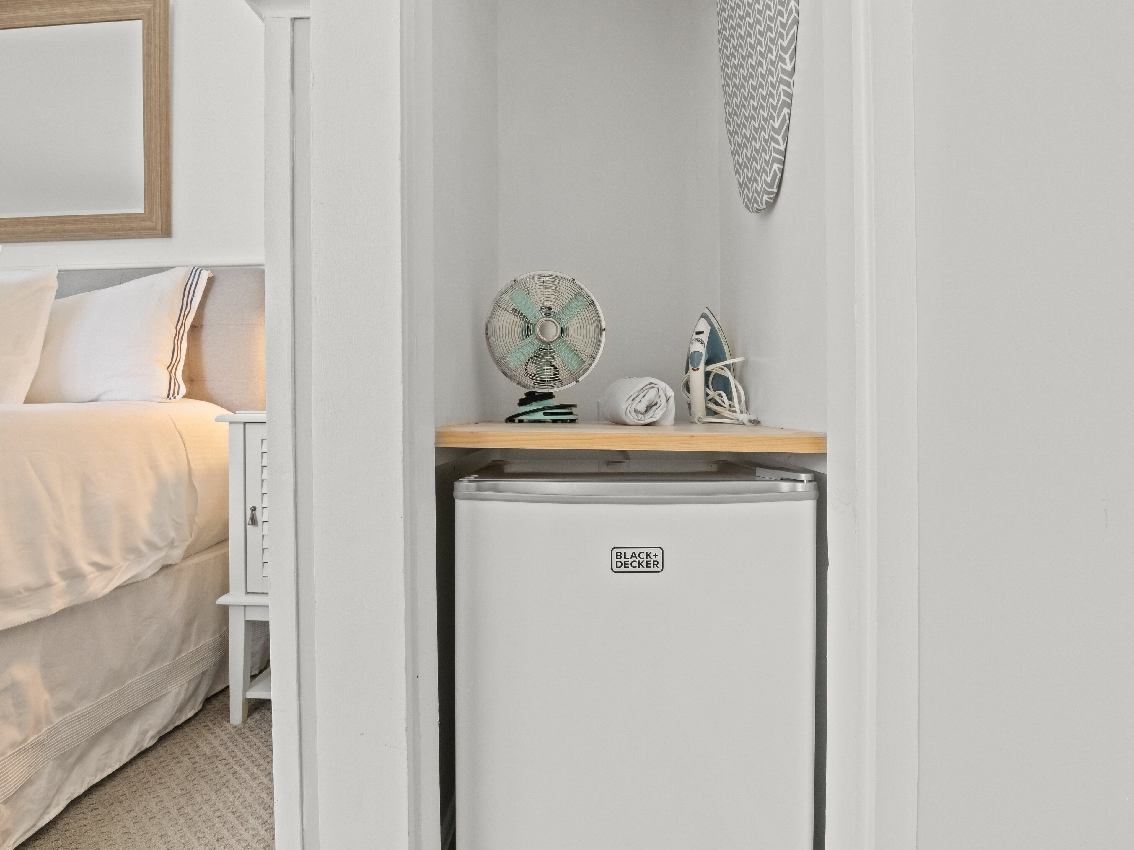 A compact kitchenette with a white refrigerator, a fan, and an iron on the countertop.