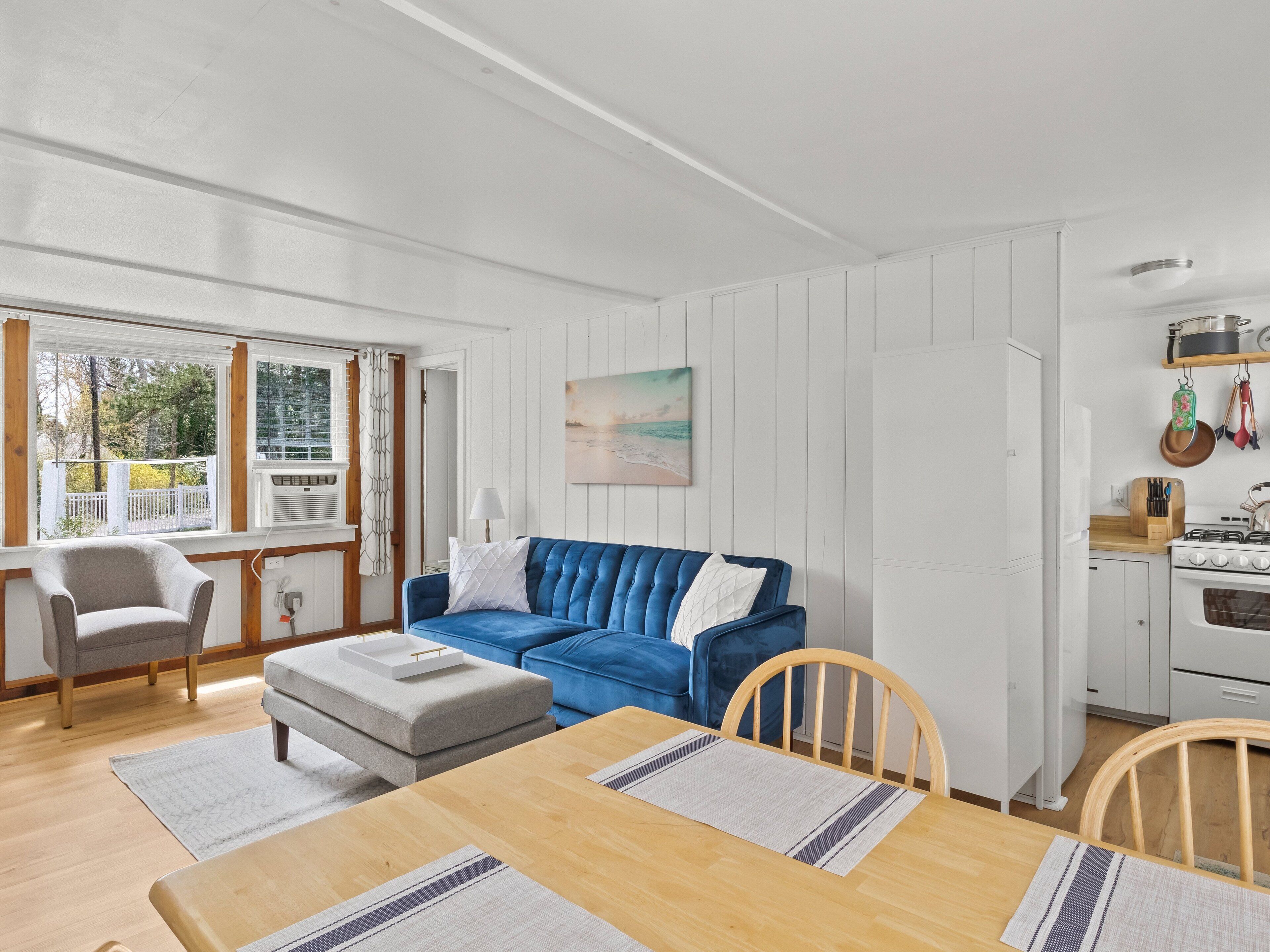 A modern living room with a blue sofa, a dining table with placemats, and a kitchen area with a stove and cabinets.