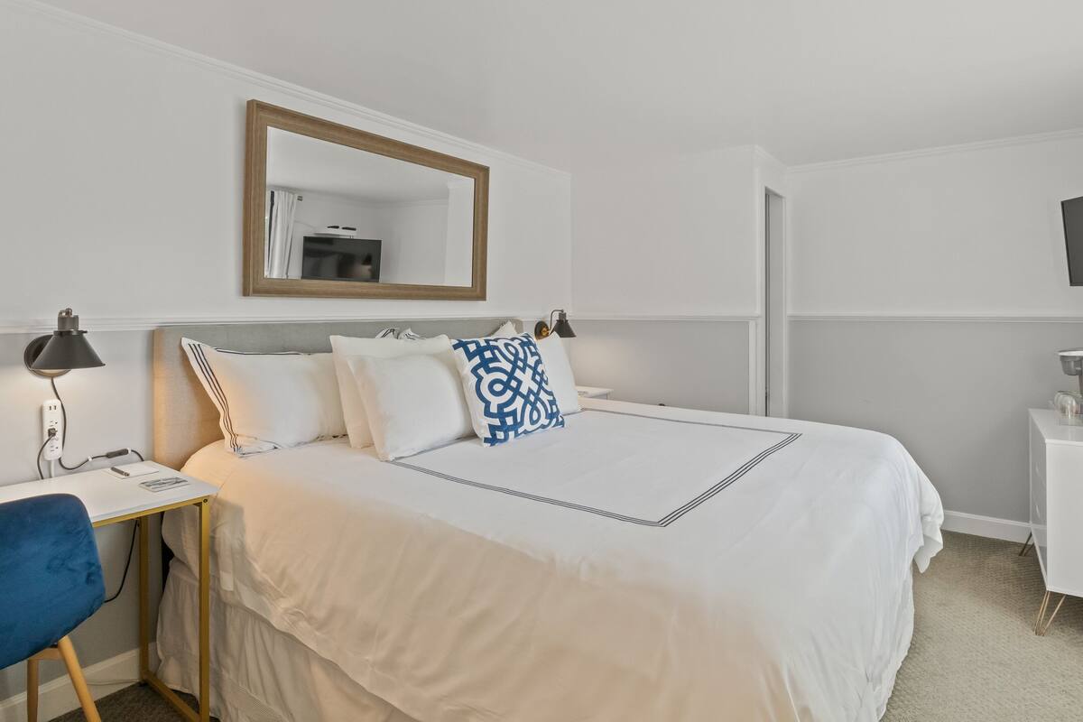 Hotelkamer met een bed, een bureau met stoel, een lamp en een spiegel aan de muur.