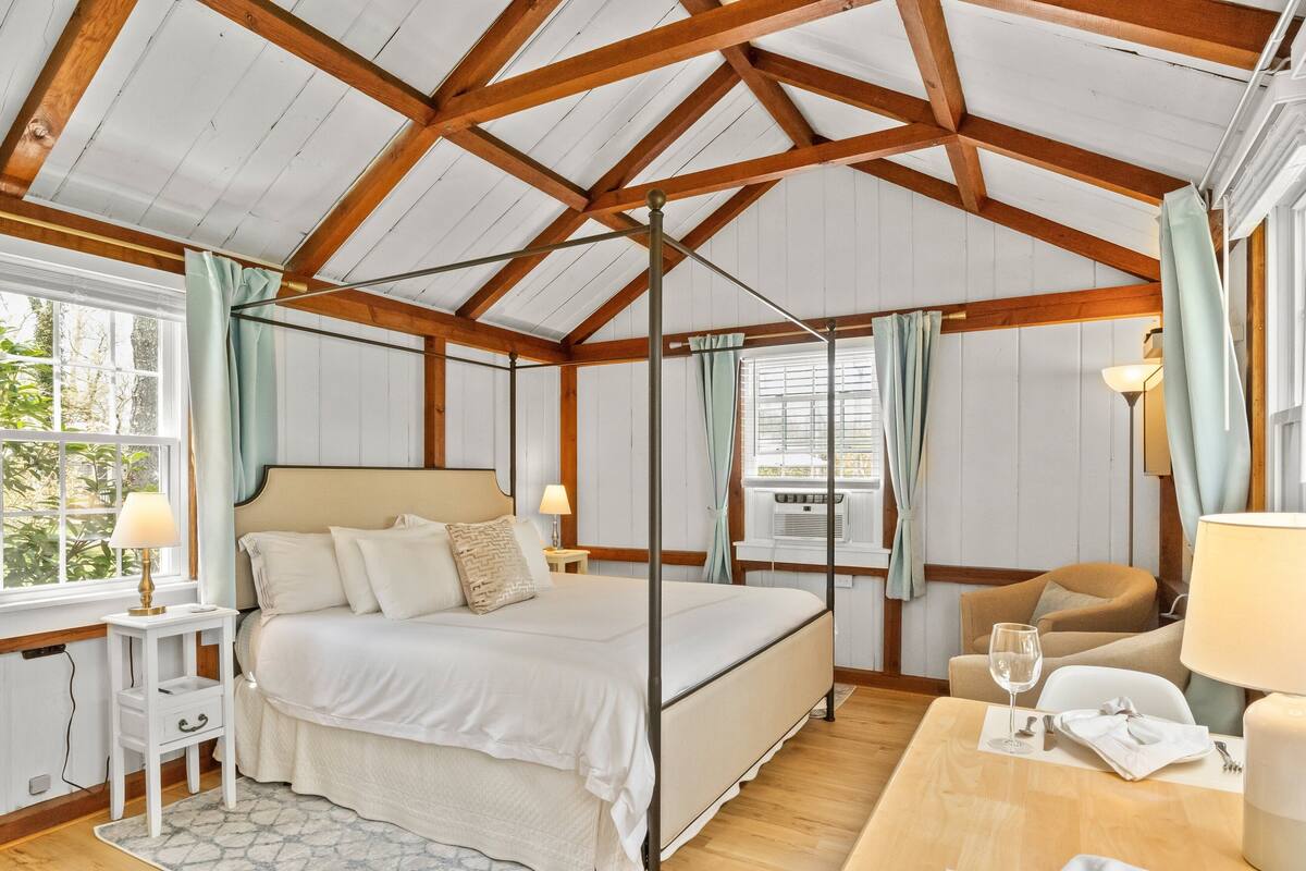 Een ruime slaapkamer met een groot bed, een houten plafond en een raam met gordijnen.