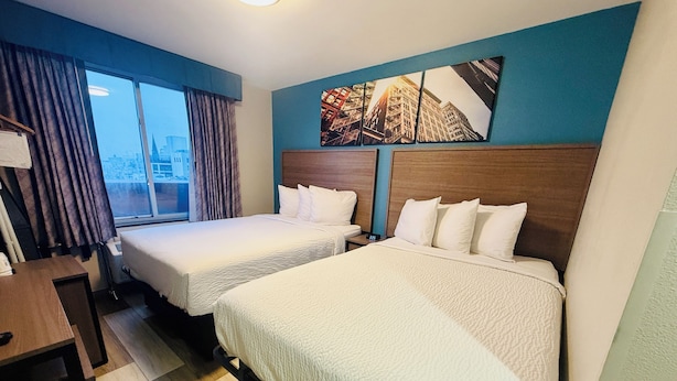 A hotel room with two beds, a desk, a chair, and a window with curtains. - Days Inn by Wyndham Brooklyn Borough Park (Brooklyn)