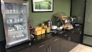 A kitchen area with a refrigerator stocked with beverages, a coffee machine, and a bread display. - Days Inn by Wyndham Brooklyn Borough Park (Brooklyn)