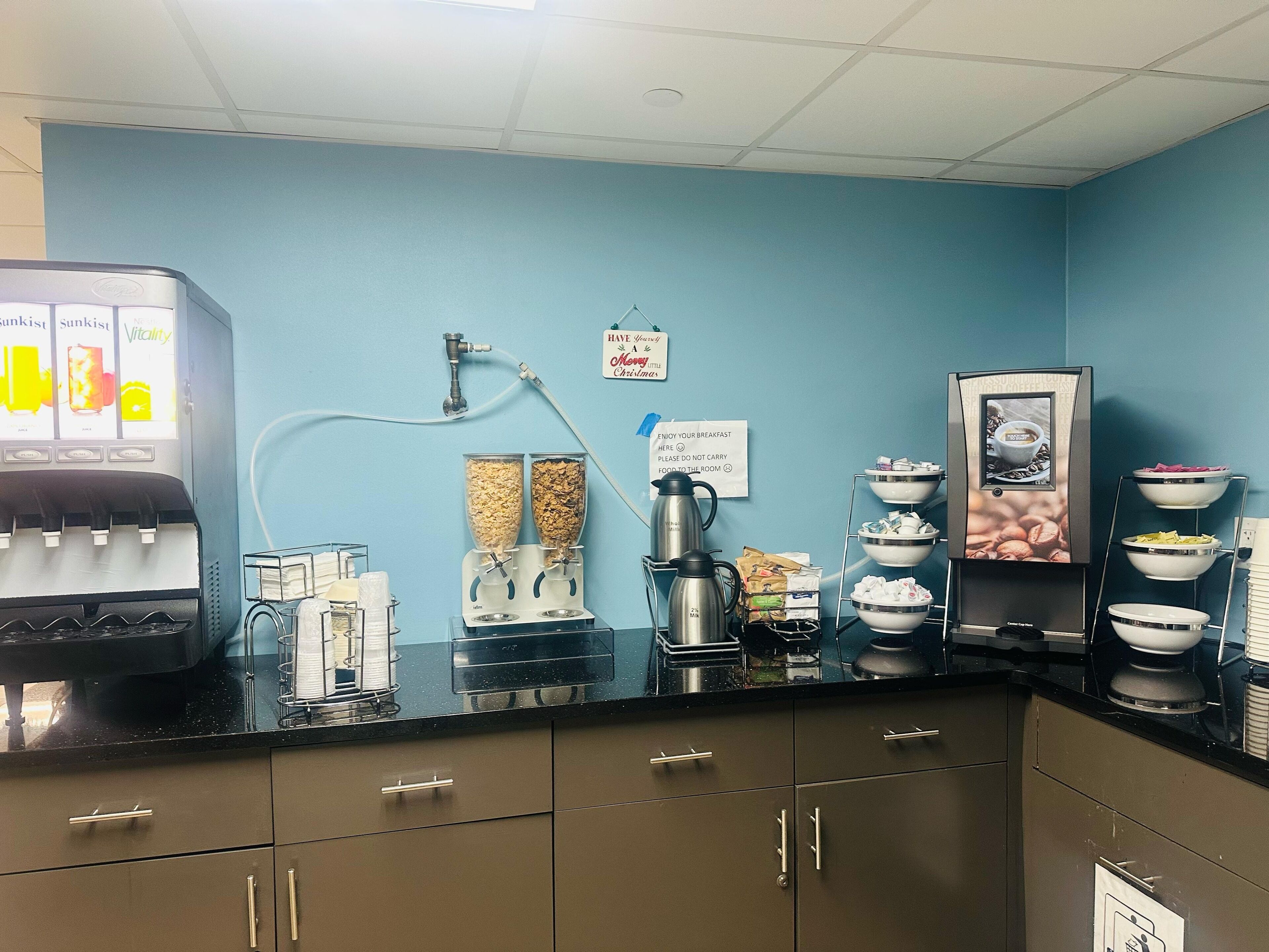Een ontbijtbuffet met een koffieapparaat, cornflakesdispensers en een koffiekan.
