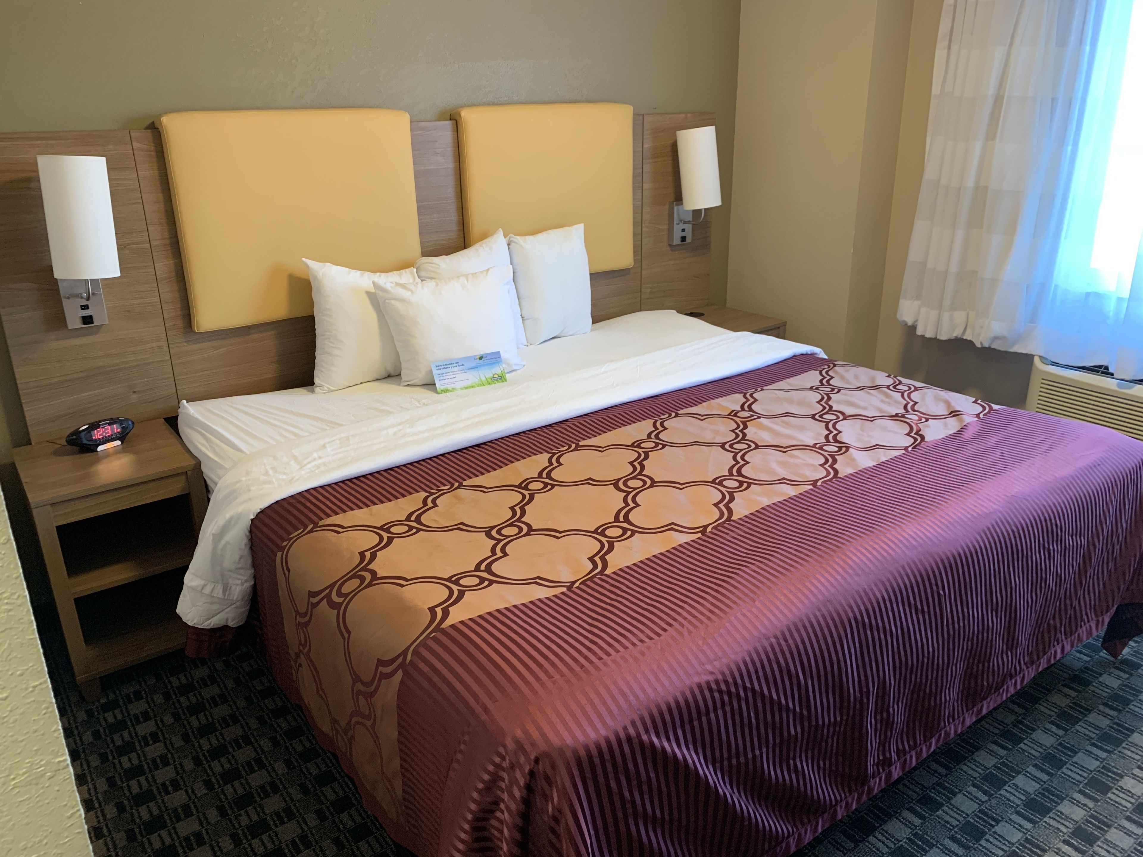 Une chambre d’hôtel avec un lit, une table de chevet, une lampe et une horloge.