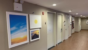 A hallway with framed artwork on the walls, doors, and a fire alarm. - Days Inn by Wyndham Brooklyn Borough Park (Brooklyn)
