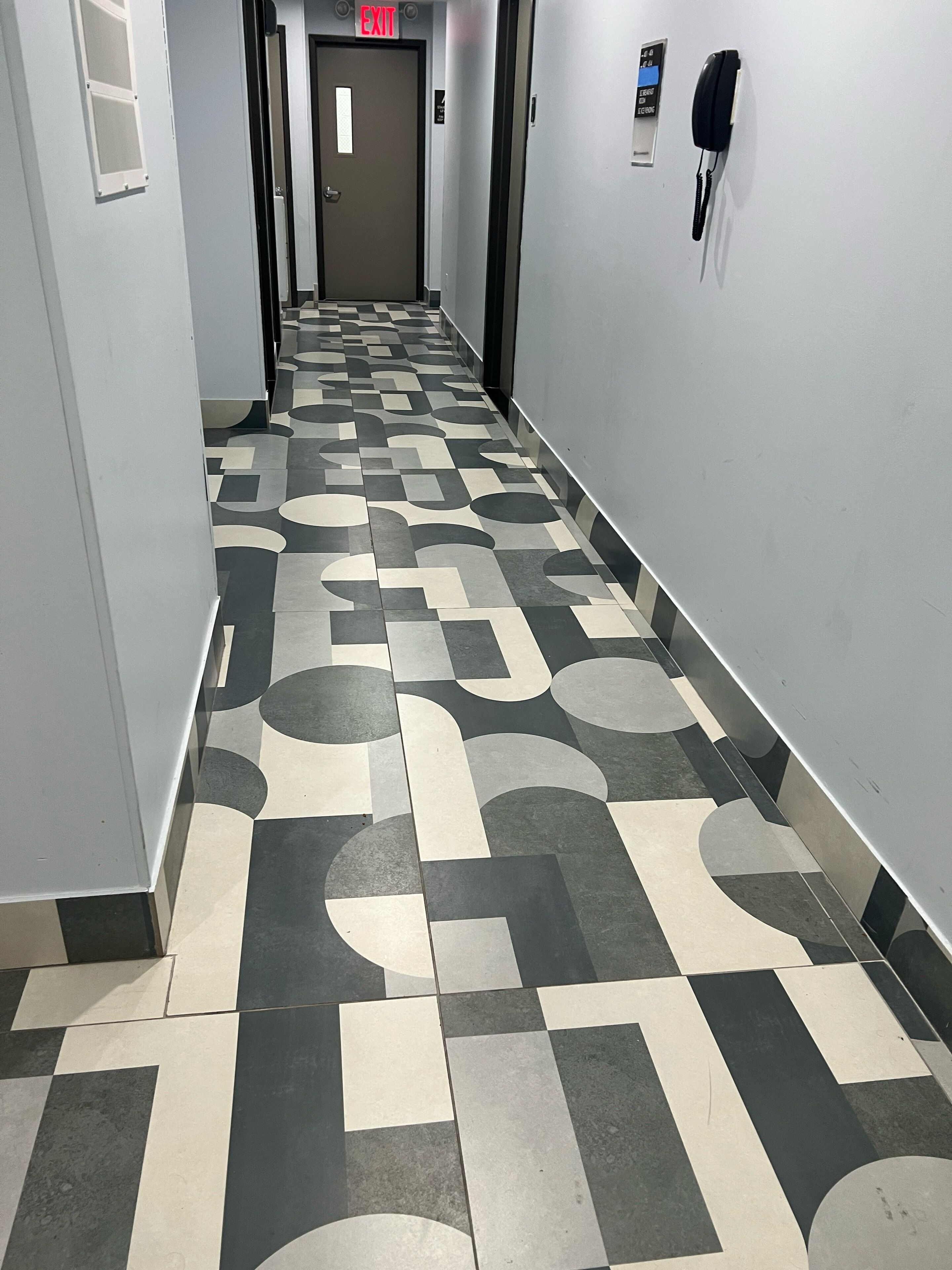 A hallway with a patterned floor, an exit sign, and a phone on the wall.