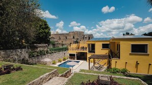 Un patio con piscina, un edificio amarillo y una antigua pared de piedra.
