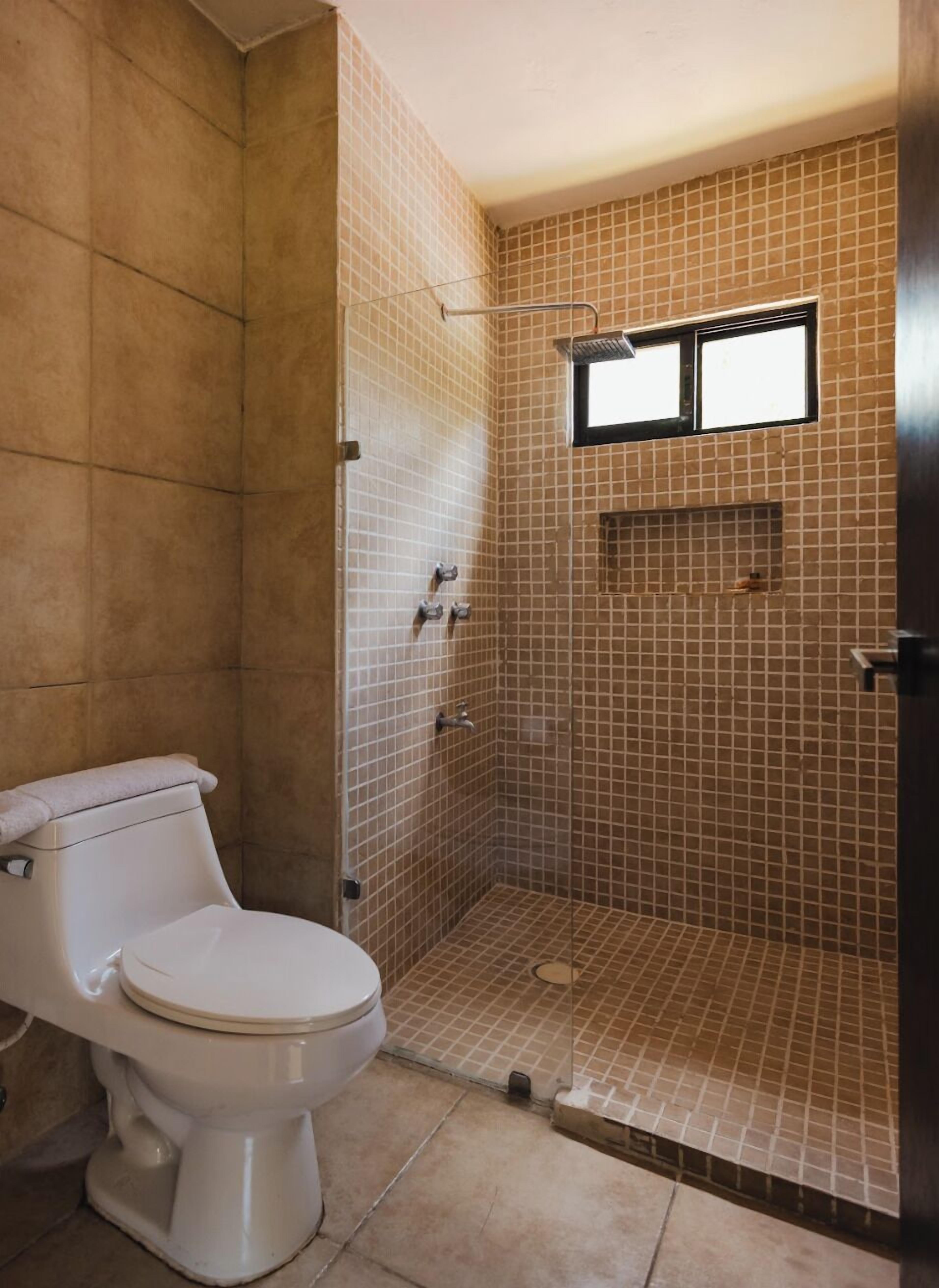 A bathroom with a toilet, a shower with a window, and tiled walls.