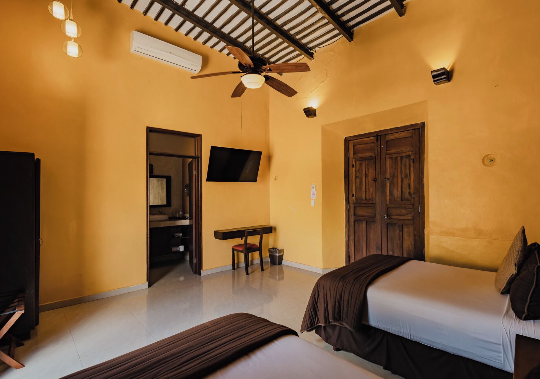Una habitación con cama, escritorio, televisor y ventilador de techo.