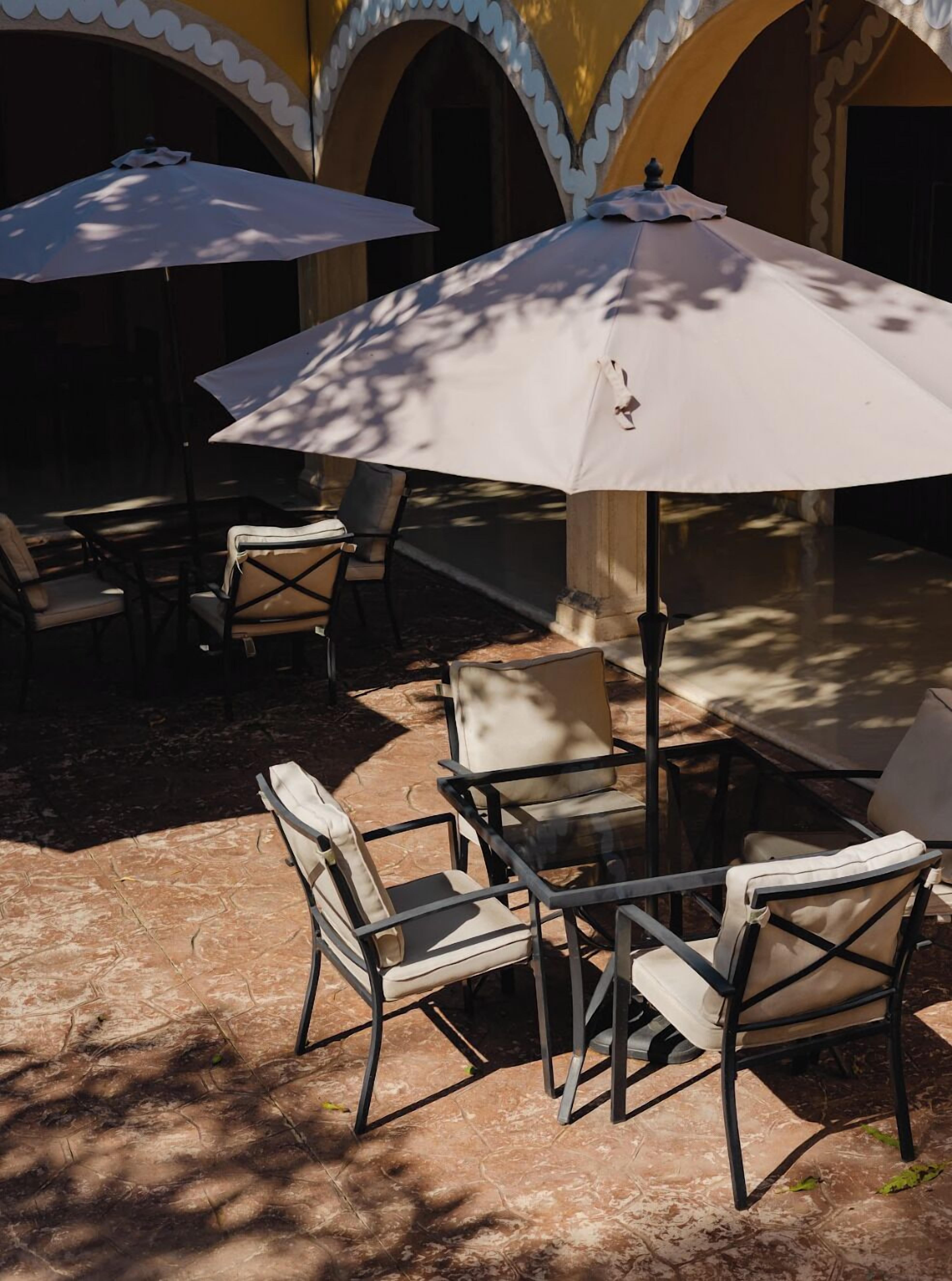 An outdoor patio with tables and chairs, covered by umbrellas, and a tiled floor.