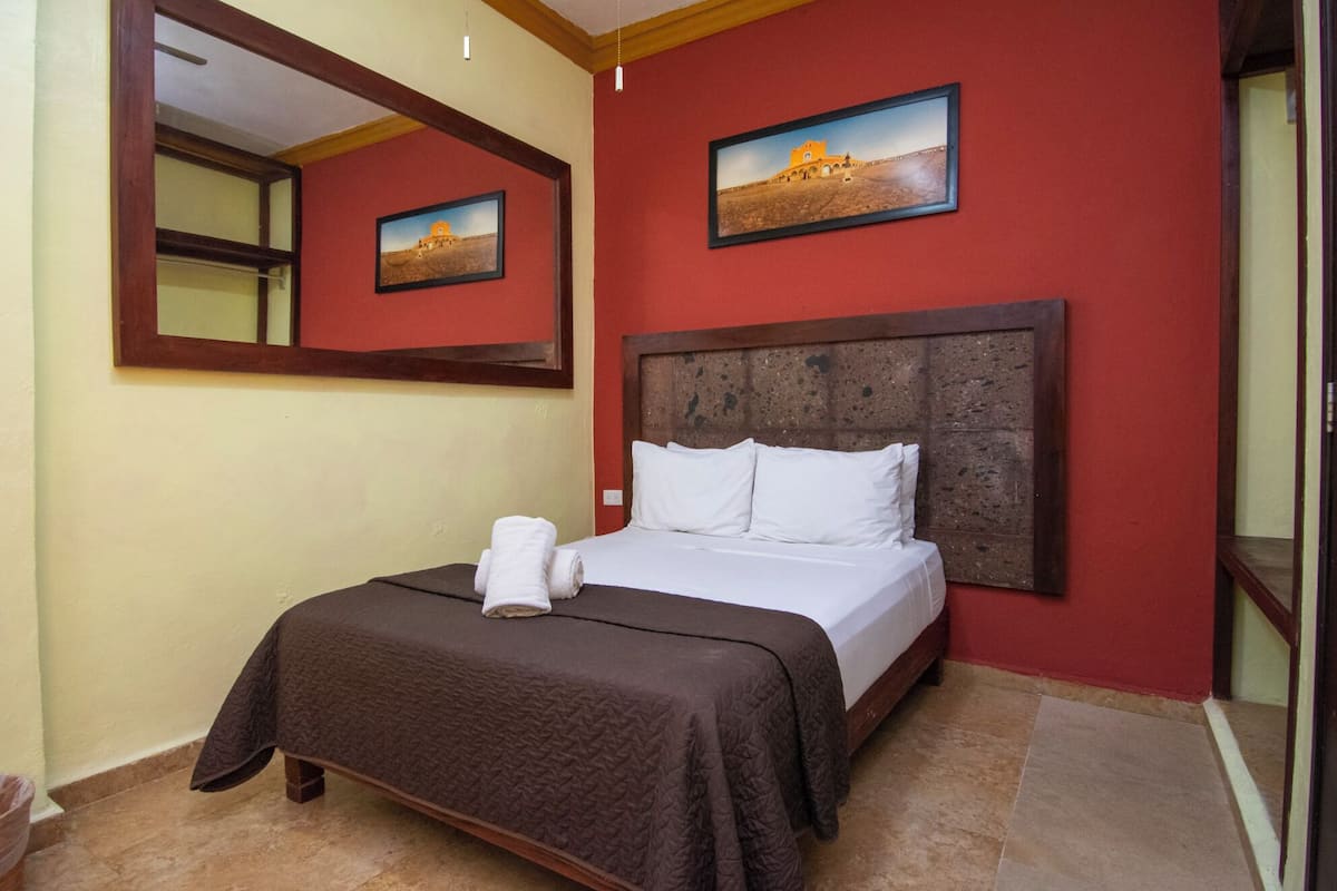 A hotel room with a bed, a mirror, and two framed pictures on the wall.