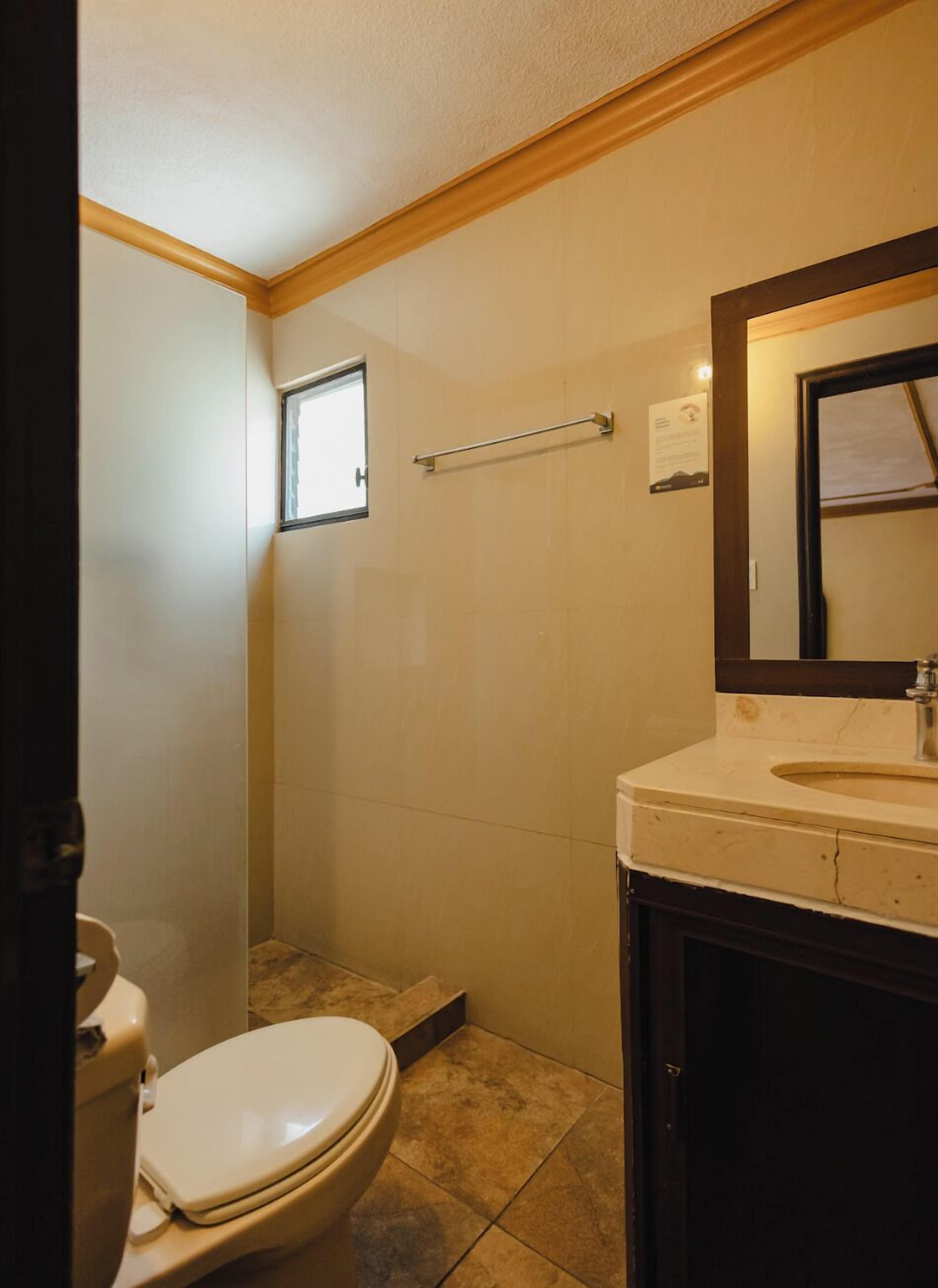 Un baño con inodoro, lavamanos, espejo y zona de ducha.