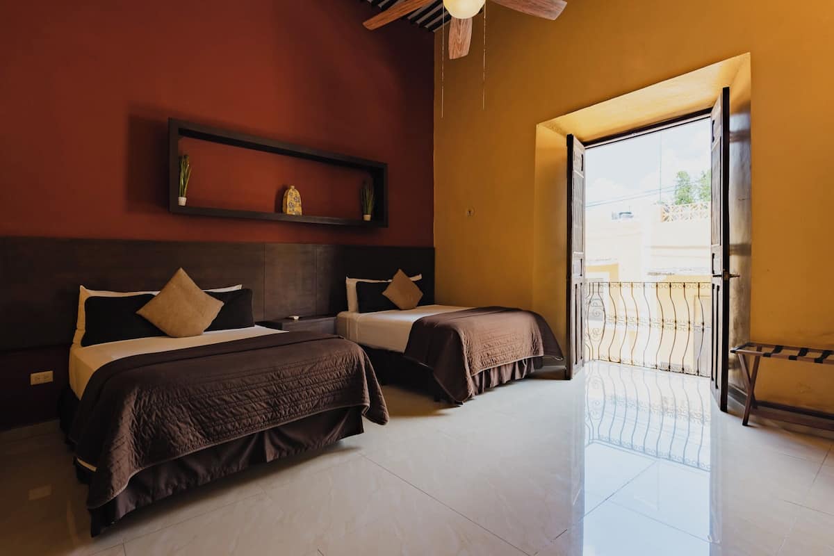 A hotel room with two beds, a wooden headboard, a shelf with decorative items, and a balcony with a metal railing.