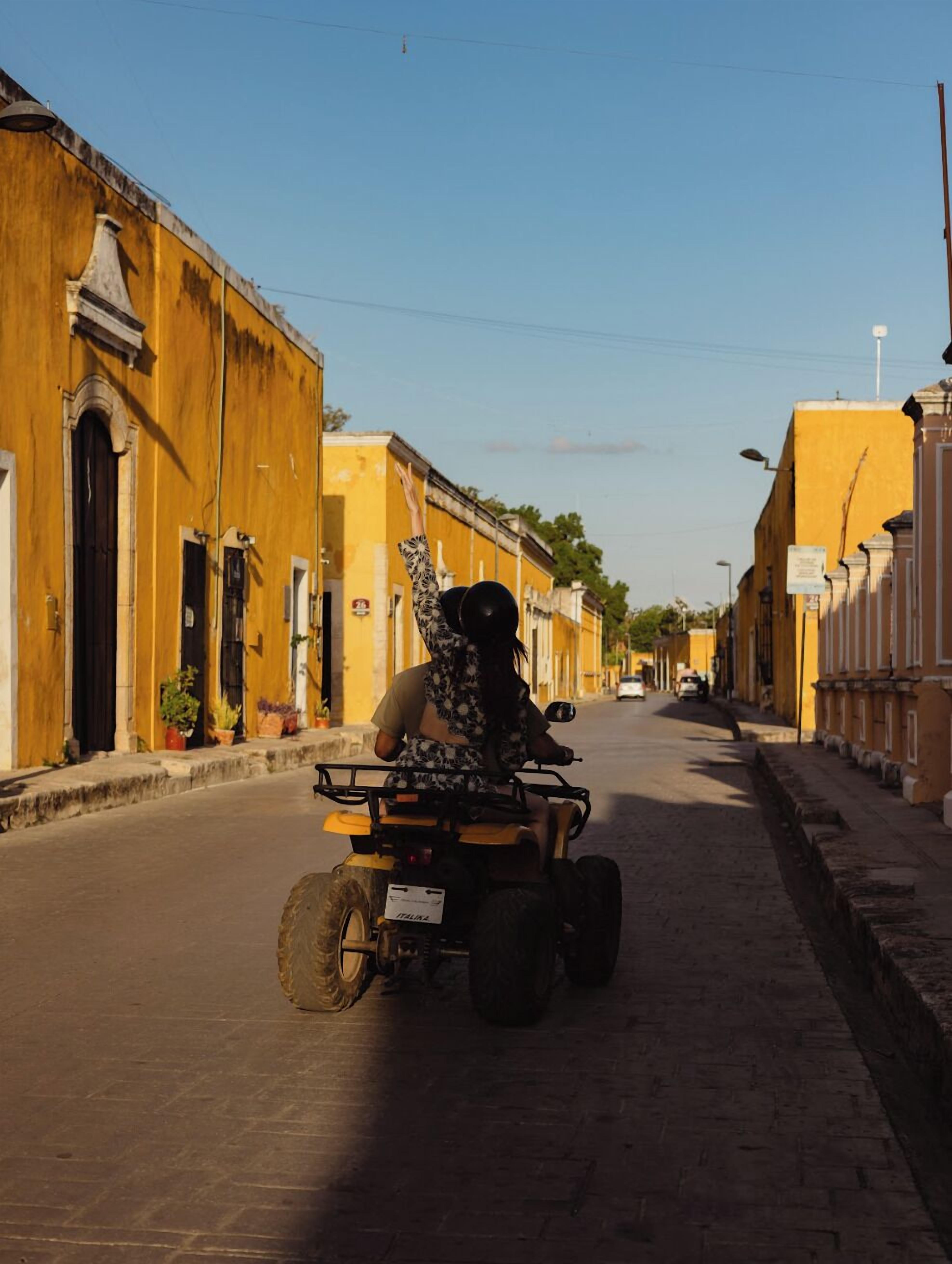 A street with yellow buildings, a person on a quad bike, and a clear sky.