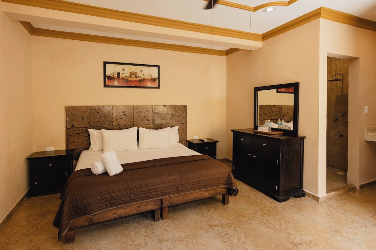 A bedroom with a bed, nightstands, a dresser, a ceiling fan, a painting, and a shower area.