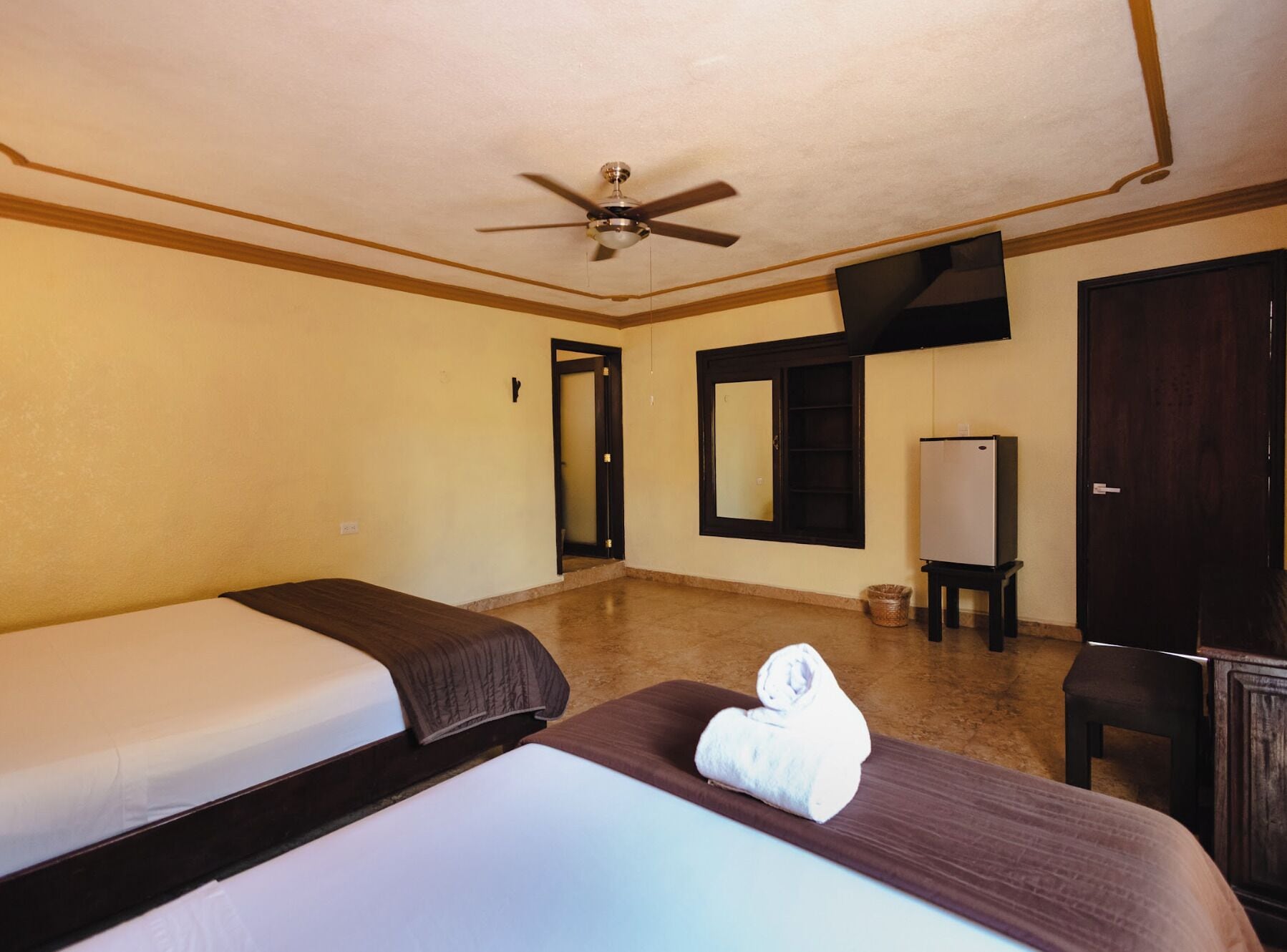 A hotel room with two beds, a ceiling fan, a television, and a wardrobe.
