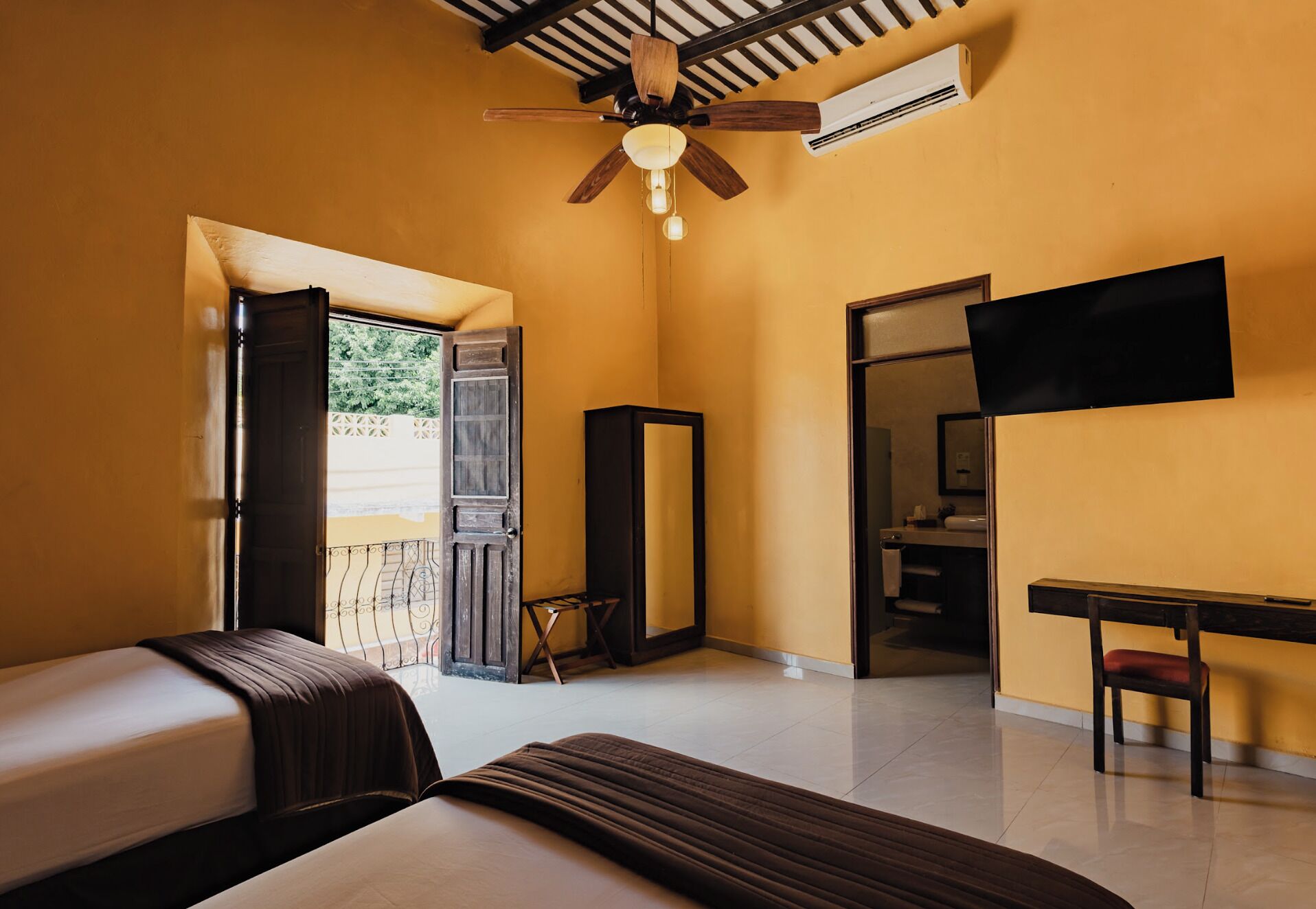 A hotel room with a bed, a desk, a TV, a ceiling fan, and an air conditioning unit.