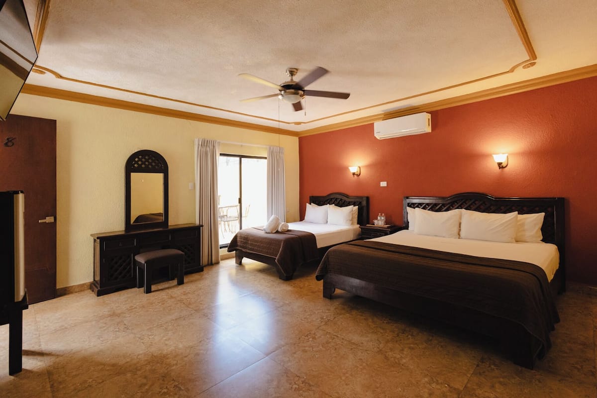 A hotel room with a bed, a desk, a chair, a ceiling fan, and an air conditioning unit.