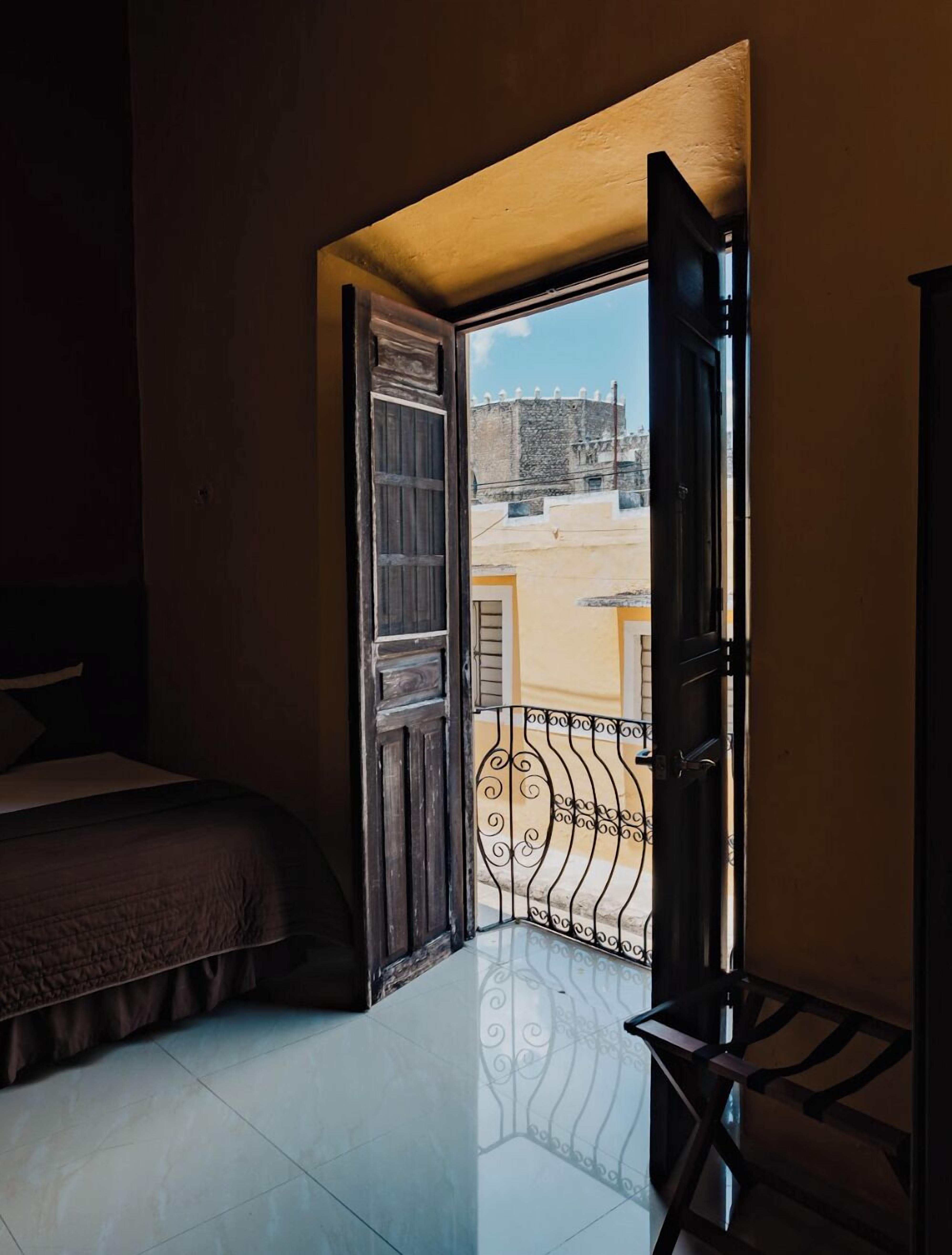 A bedroom with a bed, a door leading to an outdoor balcony, and a view of a building.