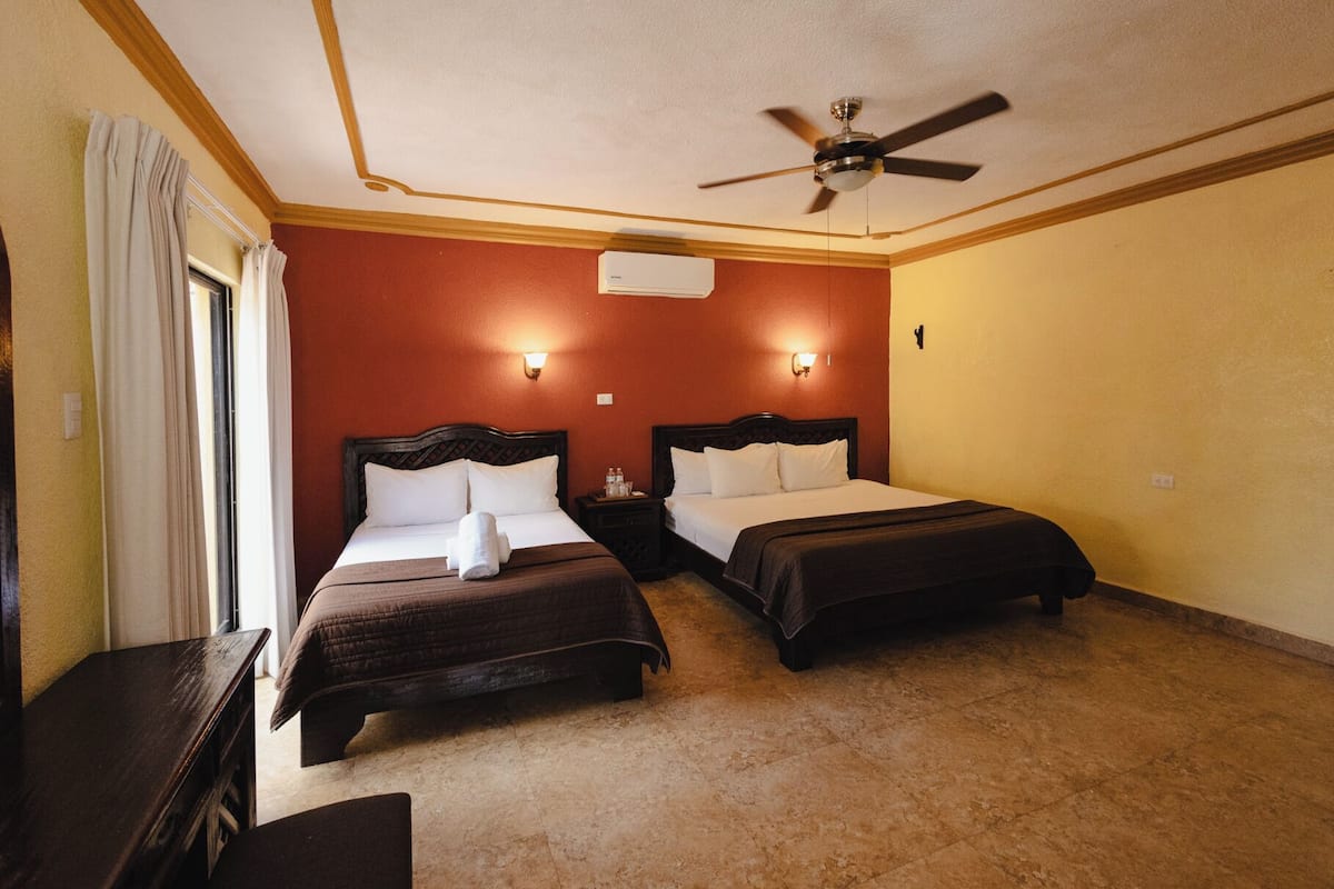 A hotel room with two beds, a ceiling fan, and a nightstand with a lamp.