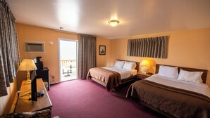 Een hotelkamer met twee bedden, een bureau met een lamp, een stoel en uitzicht op het omliggende landschap.