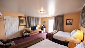 Een hotelkamer met twee bedden, een bureau met een televisie, een stoel en een raam met gordijnen.
