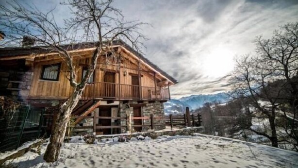 Eine Holz-Chalet mit Balkon, vor einer verschneiten Landschaft mit Bergen im Hintergrund.