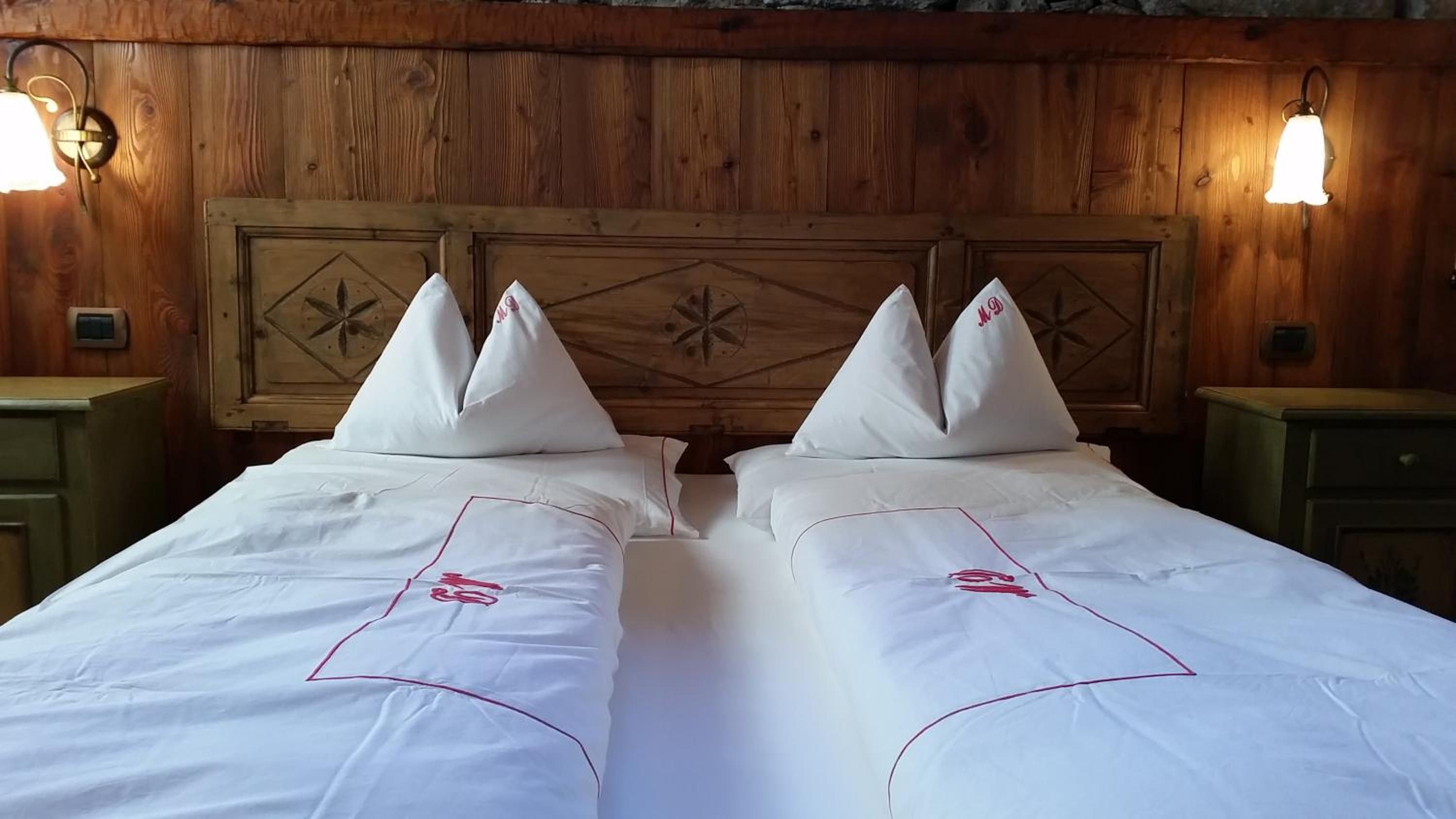 Un letto matrimoniale con lenzuola bianche e bordi rossi, due cuscini e una testiera in legno con motivo a stella.