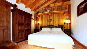 Ein Schlafzimmer mit Holzwänden, einem großen Bett, einem Holzschrank und einer schrägen Decke mit sichtbaren Balken.