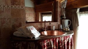 Ein rustikales Badezimmer mit einem Kupferspülbecken, einem Spiegel, einem Handtuch und einem Wasserkocher.