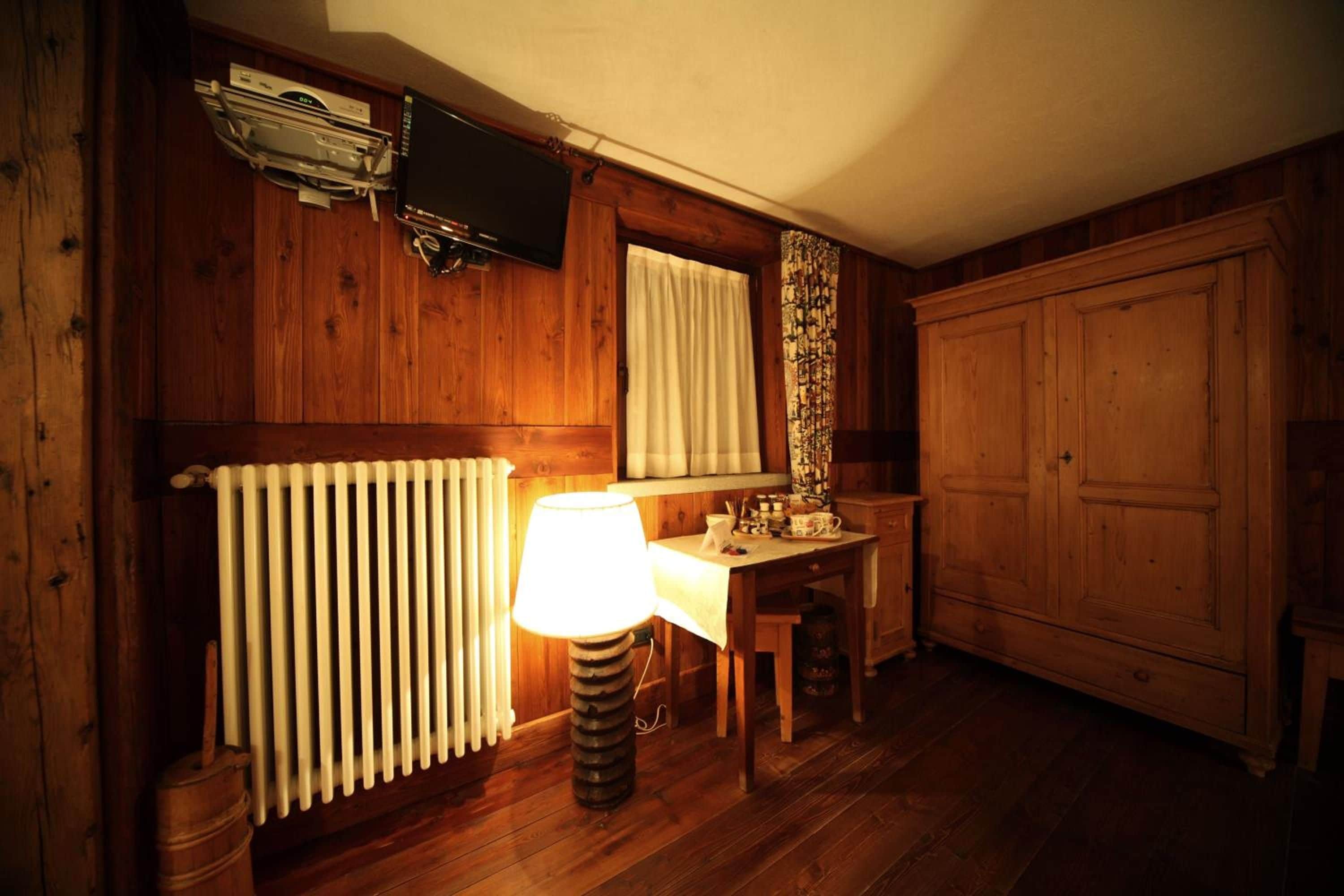 A wooden room with a radiator, a table with a lamp, a television mounted on the wall, and a wardrobe.