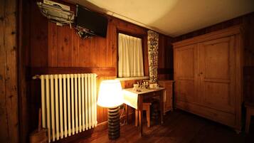 A wooden room with a radiator, a table with a lamp, a television mounted on the wall, and a wardrobe.