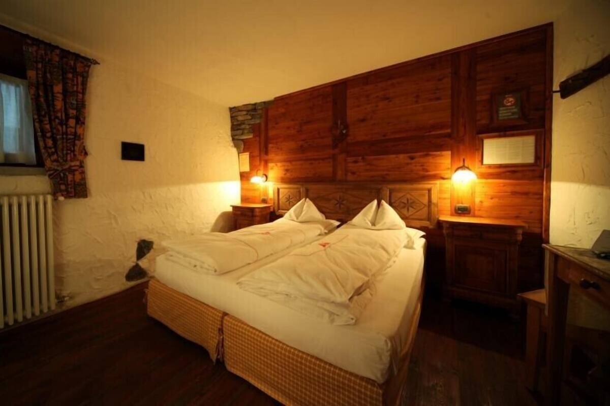 A cozy bedroom with a double bed, wooden headboard, two bedside lamps, and a window with curtains.