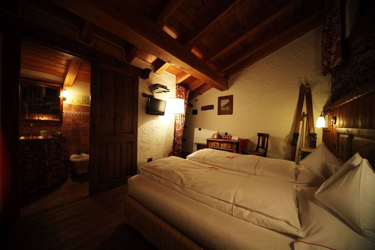 A cozy room with a wooden ceiling, a bed with white linens, a small bedside table, and a wall-mounted television.