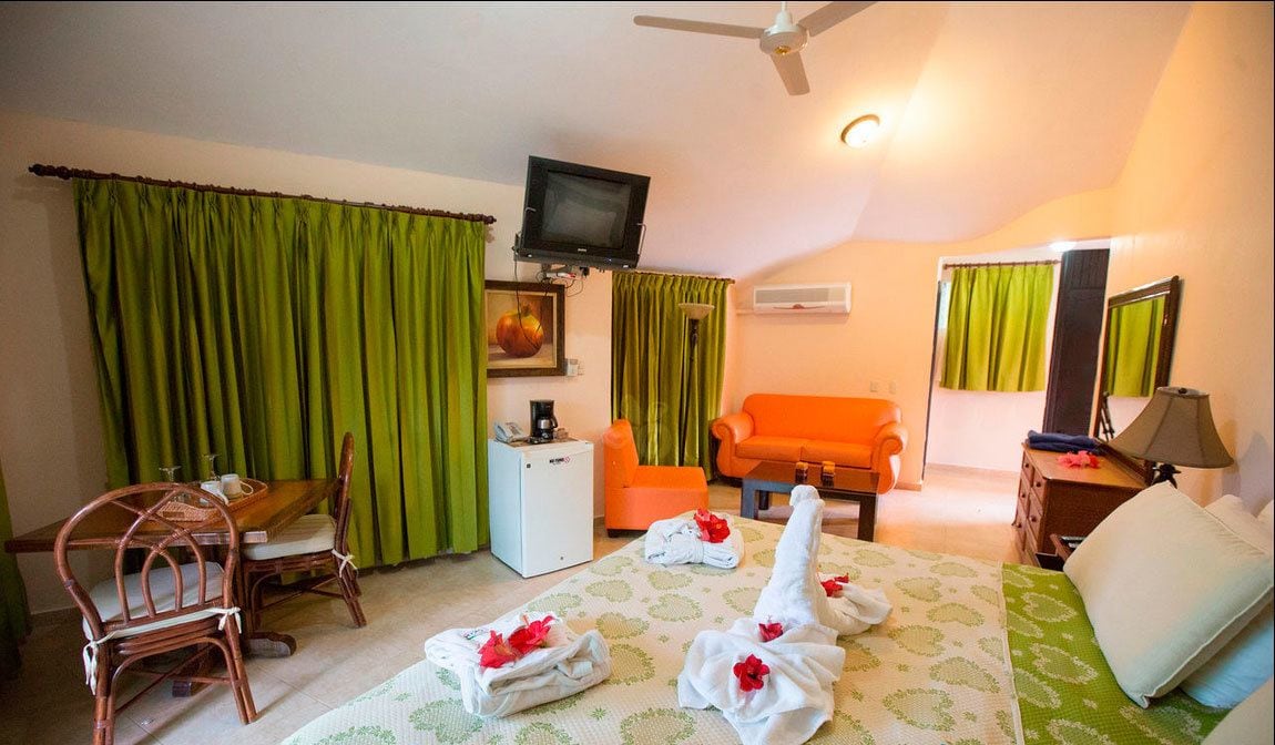A hotel room with a bed, two chairs, a small table, a television, and a desk with a lamp.