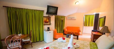 A hotel room with a bed, two chairs, a small table, a television, and a desk with a lamp.