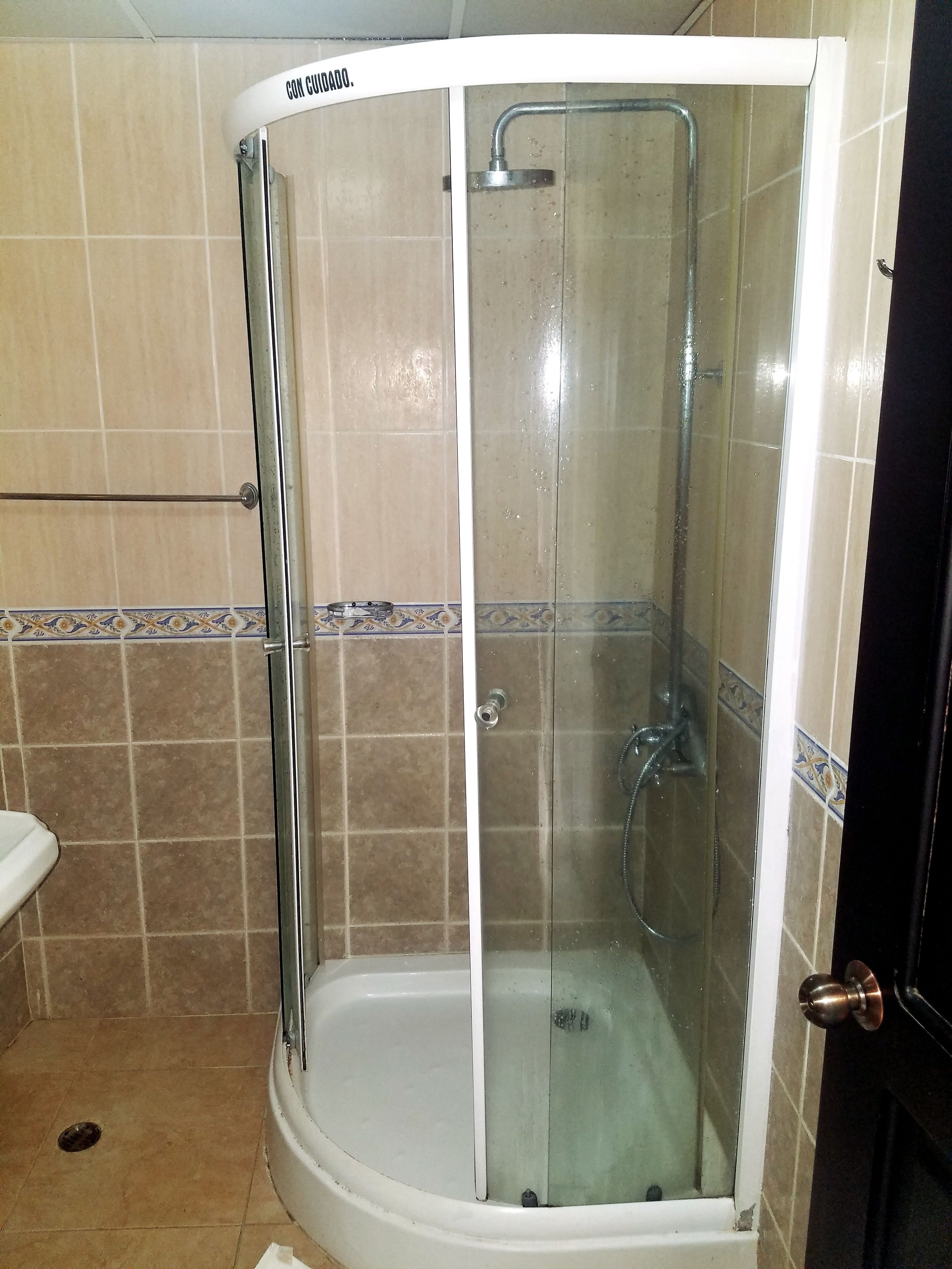 A corner shower enclosure with a glass door, a showerhead, and a handheld shower attachment.