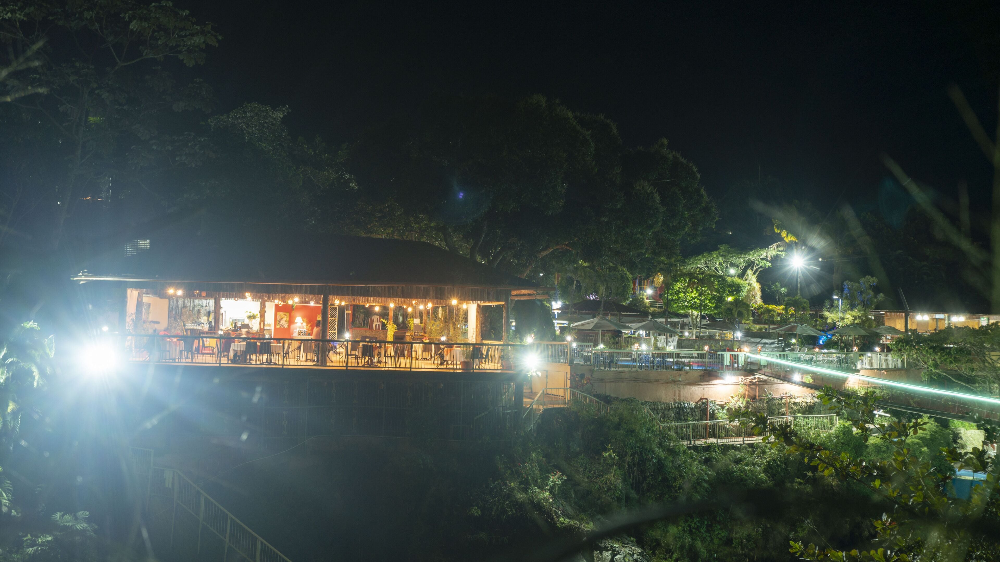 A well-lit restaurant with outdoor seating, surrounded by lush greenery.